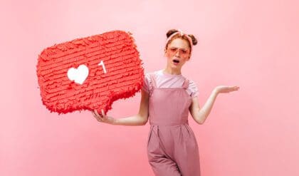 Positive lady dressed in pink overalls, t-shirt and pink accessories points finger at like sign